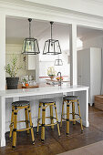 White breakfast bar with bar stools below pendant lamps with glass lampshades