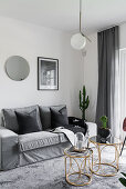 Delicate golden tables in front of sofa in grey living room