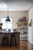 Kücheninsel mit Barhockern, Industrielampe und Metallregal, Frau vor Fenster