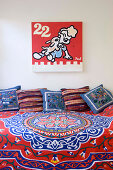 Colourful bedspread and scatter cushions on bed below comic-style artwork