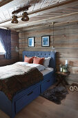 Blaues Bett mit Schubladen und Fell als Bettvorleger im Blockhaus