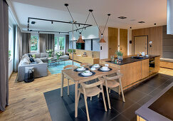 Kitchen counter with bar stools and breakfast table at one end and elegant lounge in background in open-plan interior