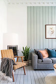 Retro Armlehnstuhl vor Kamin und graue Sofagarnitur im Wohnzimmer mit hellgrün gestrichener Holzwand