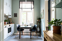 Tisch mit zwei Stühlen vor Fenster in der Küche, im Vordergrund Holztisch mit Zimmerpflanze