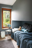 Bett mit blauer Decke und Kuscheltier, Globusleuchte auf Fensterbank im Kinderzimmer