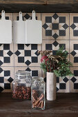 Storage jars and wintry vase of flowers against rustic tiles