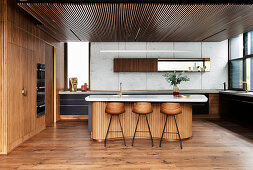 Kücheninsel mit Marmorplatte und Barhockern in offener Küche mit Holzverkleidung