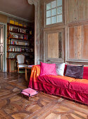 Sofa with scatter cushions and throw in shades of red on antique parquet floor