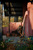 Überdachte Terrasse und Stuhl mit Fell am roten Holzhaus im Herbst