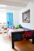 Wooden bed with colourful bed linen, row of trophies and turquoise curtain in boy's bedroom