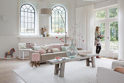 Living room in pale shades with arched windows and woman looking through French windows