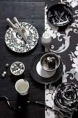 Black and white dishes on a black table with black and white wallpaper strips