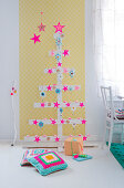 Weihnachtsbaum aus Holzlatten mit pinken Sternen vor gelber Tapete
