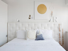 Scatter cushions on double bed with button-tufted headboard below decorations on wall