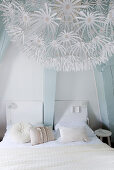 Weißes Doppelbett im Schlafzimmer mit hellblauen Balken, im Vordergrund romantische Lampe