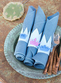 Homemade napkin rings with small crowns on blue napkins