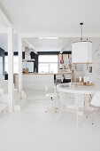 Runder Tisch mit verschiedenen Stühlen vor Kücheninsel und Treppe in weißem, offenem Wohnraum