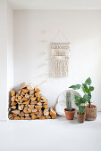 Wood storage and houseplants on a white floor, with macrame on the wall above