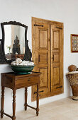 An antique side table and a mirror next to a wall cupboard with frame and panel doors