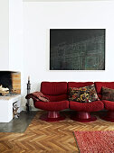 Rotes Retro-Sofa unterm schwarzen Bild neben dem offenen Kamin