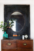 Mirror with black passe-partout frame above a chest of drawers