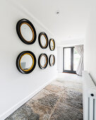 Collection of mirrors on white wall in hallway with stone-flagged floor