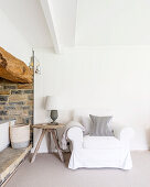Loose-covered armchair and side table next to rustic niche in converted barn