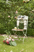 Basket of roses, chamomile and hosta leaves on lawn next to figurines of children on garden chair