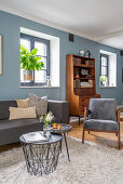 Grey sofa set, coffee table and retro dresser in living room with blue wall