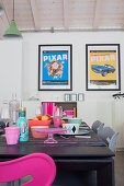 Table set with brightly coloured, kitschy crockery below framed film posters on wall