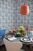 Round, set table and designer chairs in front of blue-and-white wallpaper