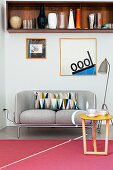 Collection of vases on retro wooden shelf above grey two-seater sofa