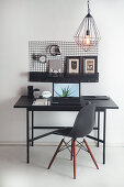 Black table and designer chair below wall-mounted organiser in work area