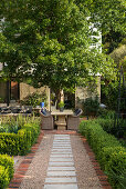 Gravel garden path leading to terrace with stone table and rattan armchairs