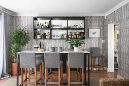 Cocktail bar in living room with tall table, upholstered barstools and mirrored shelves