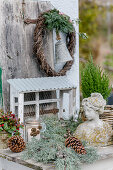 Wintry arrangement of cypress branches and pine cones around bust and wreath of creeping wire vine, yew, olive branch and bell