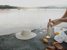 Woman opening glass of sparkling wine for picnic on shores of lake