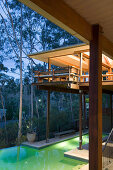 Modern, architect-designed wooden house on stilts with pool illuminated at twilight