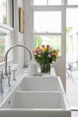 Vase of roses next to white double sinks with tap fittings in kitchen