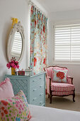 Pale blue chest of drawers and pink-striped armchair in girl's bedroom