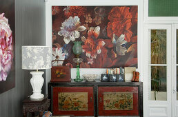 Oriental cabinet below floral artwork and table lamp on antique side table