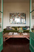 View through open, green double doors to coffee table and moss-green sofa