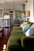 Offener Wohnraum im Vintagestil mit moosgrünem Sofa und Edelstahlküche im Hintergrund