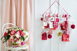 DIY-Adventskalender in Weiß, Rot und Rosa davor Blumenbouquet auf Stuhl