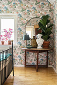 Fiddle leaf fig and bust on semicircular table against floral wallpaper