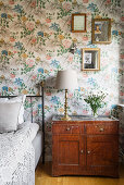 Old bedside cabinet in bedroom with floral wallpaper