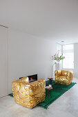 Goldene Sessel auf grünem Teppich vor eingebautem Kamin