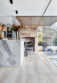 Marble island counter in open-plan kitchen with wooden floor and glass wall