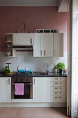Küche in Altbauwohnung mit weißen Schränken, Metrofliesenspiegel und altrosafarbenen Wänden