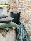Velvet cushions and blanket in shades of green against brick wall